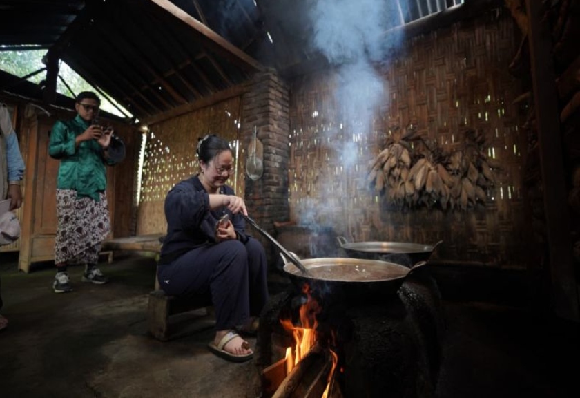 Seorang wisatawan asal Tiongkok mencoba cara memasak tradisional. 